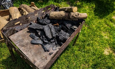 A pile of wood is on a grill, and the grill is on a grassy area. Scene is relaxed and casual, as it is a backyard barbecue or a picnic