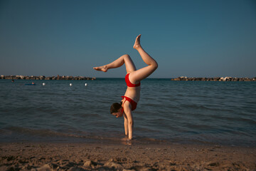 Energetic teenager girl doing handstand on the beach