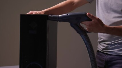 A man cleans a computer case with a vacuum in a bright room, stressing workspace tidiness