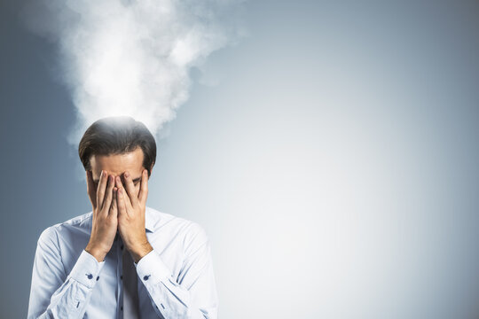 Stressed businessman with steam rising from head symbolizing burnout and overwork under pressure in corporate life on light blue background.