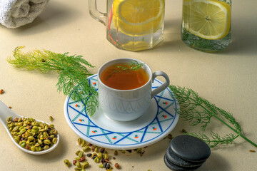 Fennel tea served in a white cup and saucer, accompanied by fennel seeds, lemon water in glass...
