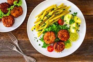 Fried chicken meatballs with boiled potatoes and wax beans on wooden table