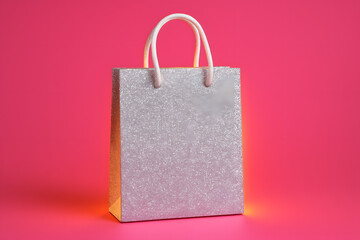 Sparkling shopping bag on vibrant background: A glistering silver shopping bag stands out against a vivid pink background, ideal for promotion, luxury purchase, gift-giving occasion.