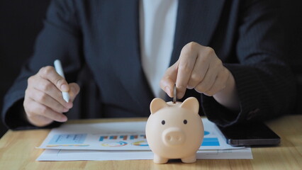 businesswoman picks up coins and puts them into a piggy bank, representing smart money saving,...