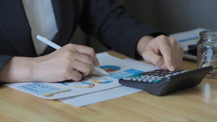 businesswoman is calculating financial figures using a calculator at her desk. financial planning,...