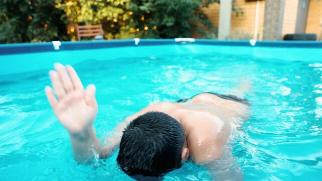 boy swimming in backyard pool with blue water summer day outdoor activity brick house and green garden on background concept of fitness swimming