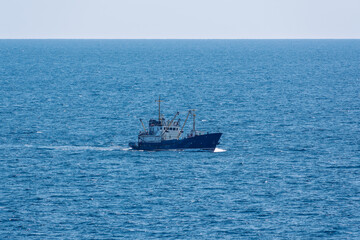 Fishing boat in blue sea and clear sky with birds flying overhead.