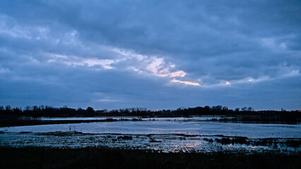 Evening cloudscape witb dark blue rainclouds and orange glow over a wetlands landscape in Bourgoyen...