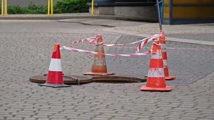 Opened Sewer Manhole with Metal Lid Secured with Street Roadworks Traffic Cones and Protective Tape as Safety Precaution