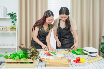 Two asian woman study online in the classroom making sandwich together in the home kitchen. Homemade and Learn online concept	