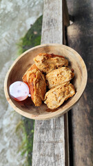 Tahu walik. Crispy browned tofu walik served in a natural wooden bowl with spicy chili sauce, with a blurry river flowing in the background. Menu at an outdoor cafe.