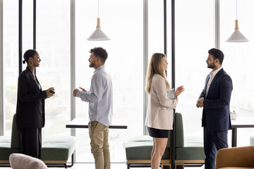 Two couples of business professionals of diverse gender age ethnicity talk standing separately by tables at creative workspace. Personal bank managers meet customers to give individual consultations