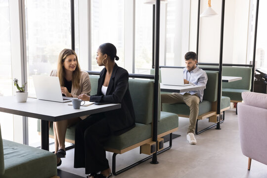 Flexible non office space for work and study. Busy diverse multicultural people sit at desks in glass cabins at cyber cafe or collaborative coworking zone learn meet clients do business as freelancers