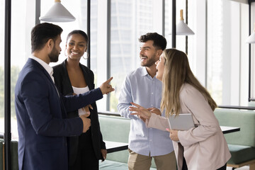 Warm relationships at workplace. Friendly international team 4 diverse employees colleagues gather together at break time chatting laughing having fun in coworking office enjoy informal communication