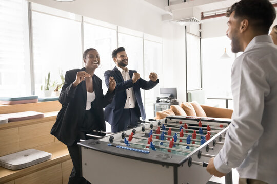 No matter who scores together we win. Overjoyed excited corporate employees table football players dance scream celebrate success scoring goal winning game with support laughter joy from opposite team - Powered by Adobe