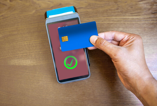 Clerk accepting a contactless blue credit card payment using nfc technology from a customer in a cafe or store. Hands of man tapping card machine reader to process cashless transaction for a purchase