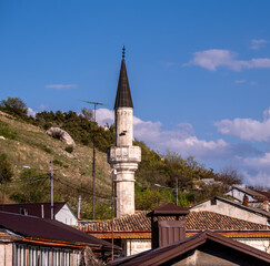 The tall minaret of the mosque against the backdrop of mountains on a summer day.