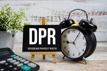 DPR Dividend Payout Ratio text with alarm clock and calculator on wooden background