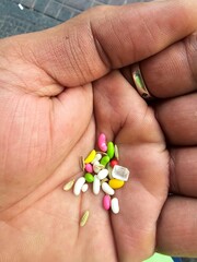 A vibrant close-up of a hand holding colorful, sugar-coated fennel seeds (saunf) and sugar crystals, a popular Indian after-meal digestive and sweet. Perfect for cultural or food-related themes.
