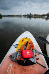 On the back of a paddle board, perched securely, there is a bright red first aid kit resting...