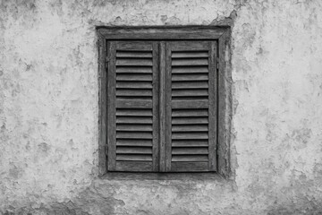 Old weathered window with wooden shutters and a rough textured wall in monochrome