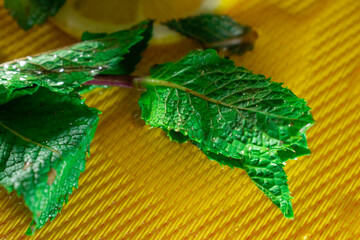 Refreshing summer close-up of mint leaves and lemon on a yellow background. Zesty and cool, ideal...