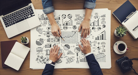 Overhead view of business meeting with sketches, laptop, and camera on a wooden table top surface