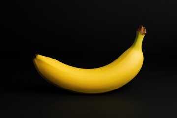 A yellow banana resting on a dark surface against a dark backdrop