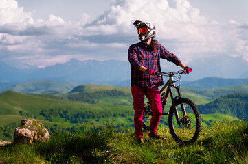 Athlete rider in bicycle helmet on his bike standing and resting before descent in mountains...