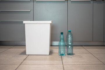 Plastic bottles next to a trash bin. Sorting plastic for easier recycling of waste.