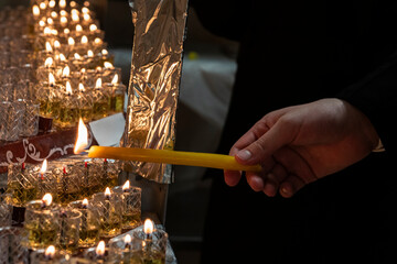 An Orthodox, haredi, Jewish man uses a long, wax, yellow taper candle to light a Hanukkah menorah...