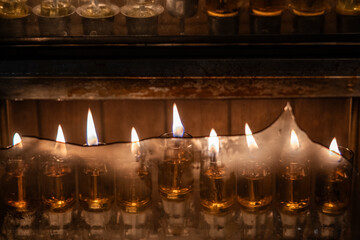 The flickering flames of burning Hanukkah candles in a menorah behind a strip of broken glass on...