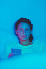 Teen girl in bed looking at smartphone in blue and pink light at night