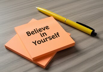 A bright orange "Believe in Yourself" sticky note with a yellow pen on a wooden desk.