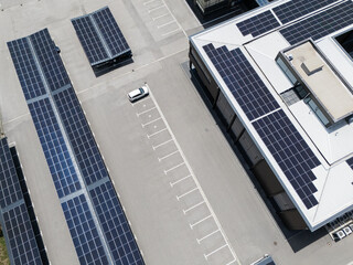 Aerial view of building with solar panels on a roof and parking space with solar canopies
