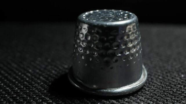 Close-up of a vintage metal thimble on textured dark surface with moody lighting and shadows