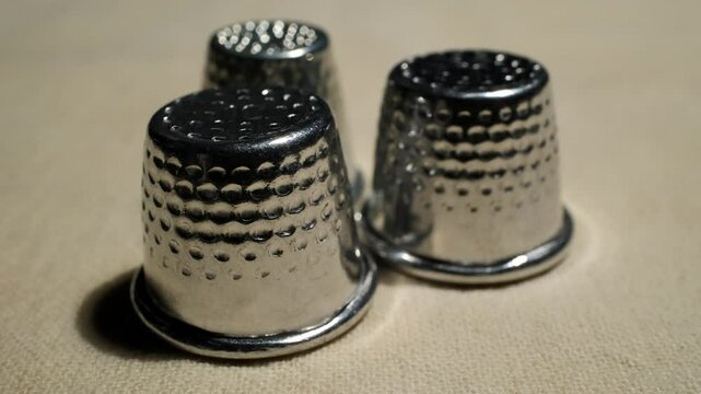Close-up of shiny metallic thimbles arranged on a textured beige fabric surface in soft natural light