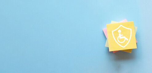 Disability insurance reminder concept. A sticky note with a protection shield and wheelchair icon,...