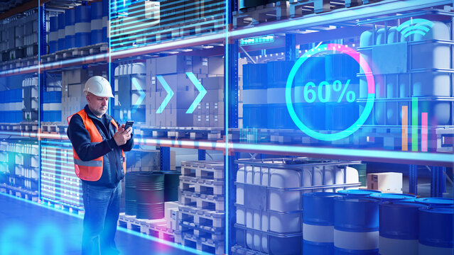 Engineer in safety gear checks smart inventory data on smartphone in automated warehouse with barrels and containers. Activity: Smart logistics, warehouse management.