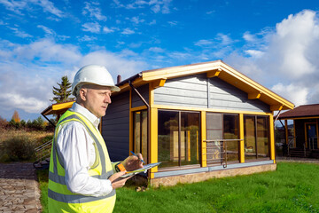 Man builder near finished house. Construction of country cottage. Man inspector supervises...