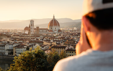 A tourist taking a photo of Cattedrale di Santa Maria del Fiore in Florence at sunset from a famous...
