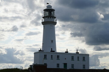 A historic white lighthouse standing tall under a dramatic cloudy sky in Flamborough, North...