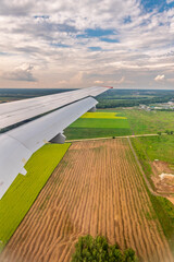 View of airplane wing, blue skies and green land during landing. Airplane window view.