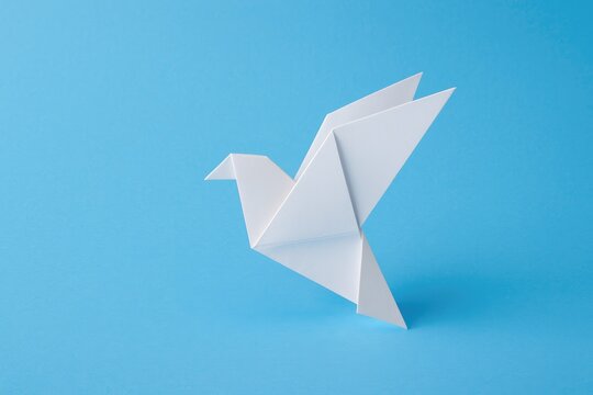 Blue background with a white folded paper bird symbolizing peace
