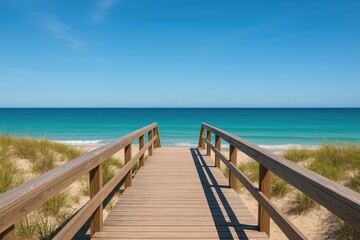 Sunlit wooden pathway leading to the shoreline on a clear blue sky day