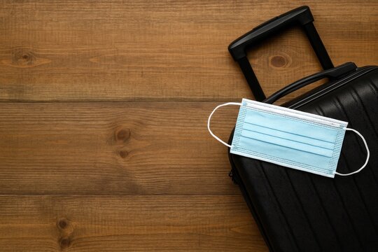 Travel essentials setup on a wooden surface featuring a suitcase and face mask during times of pandemic with space for notes