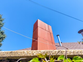 A red brick chimney is on a roof. The chimney is tall and has a pointed top. The sky is blue and...