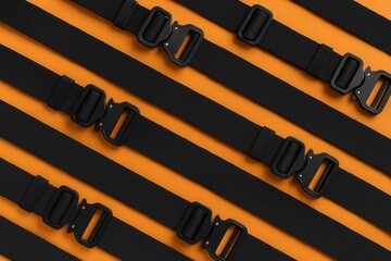 Bird's-eye view of multiple black belts featuring a quick-release metal buckle and belt loop on an orange surface.