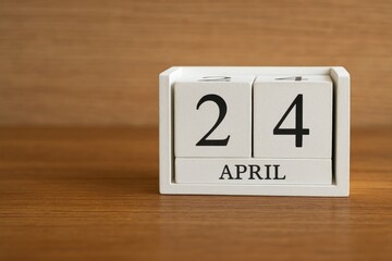 Detailed shot of a white wooden calendar featuring black dates, set against a blurred wooden desk and wall backdrop in an office environment with ample space for notes, focusing on the calendar