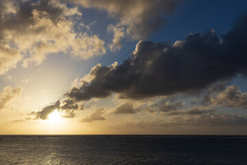 A golden sun setting over a tropical island reef featuring moody clouds in a dramatic sky.